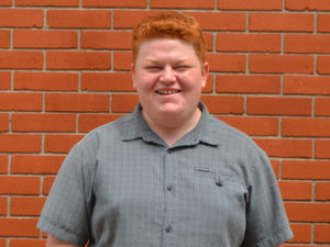 A man with red hair standing in front of a brick wall.
