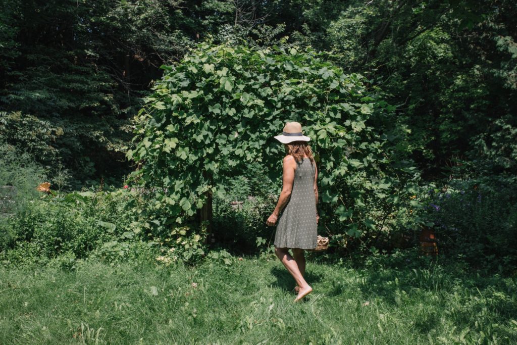 A woman in a hat walking through a garden.