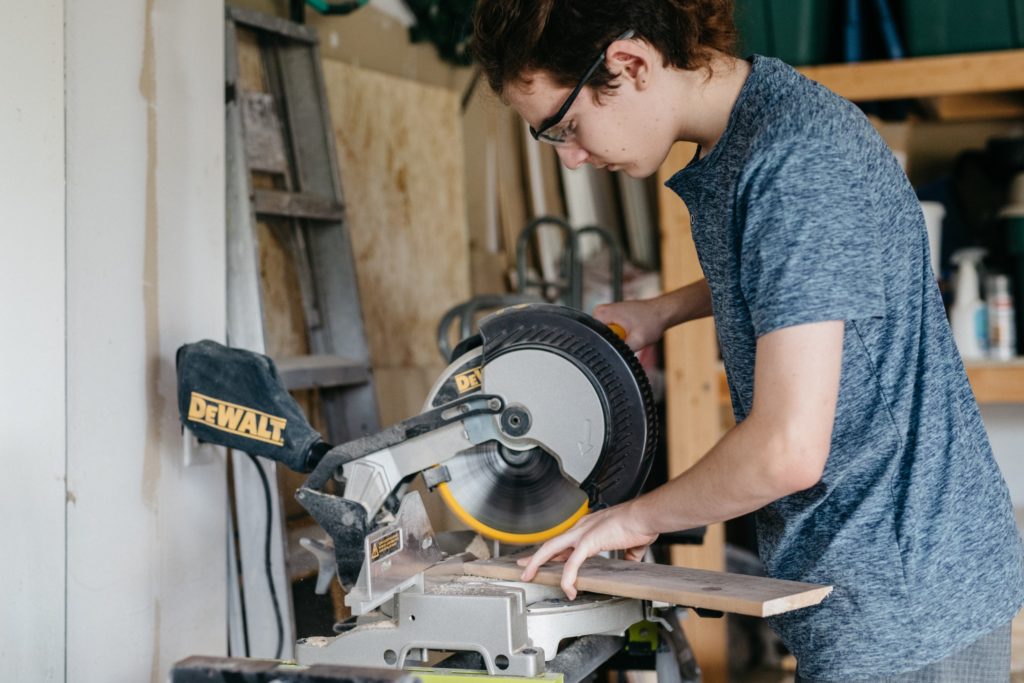 A young man using a circular saw in his garage.