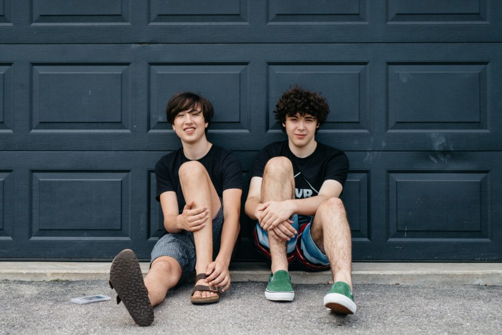 Two young men sitting in front of a garage.