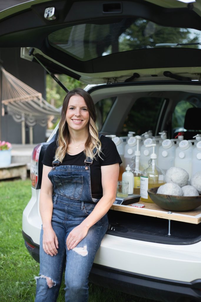 A woman in overalls with her products in the trunk of a car.
