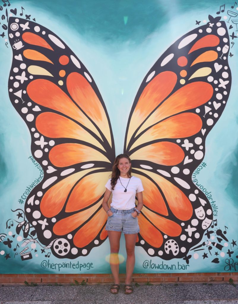 A woman in shorts standing in front of a butterfly mural.