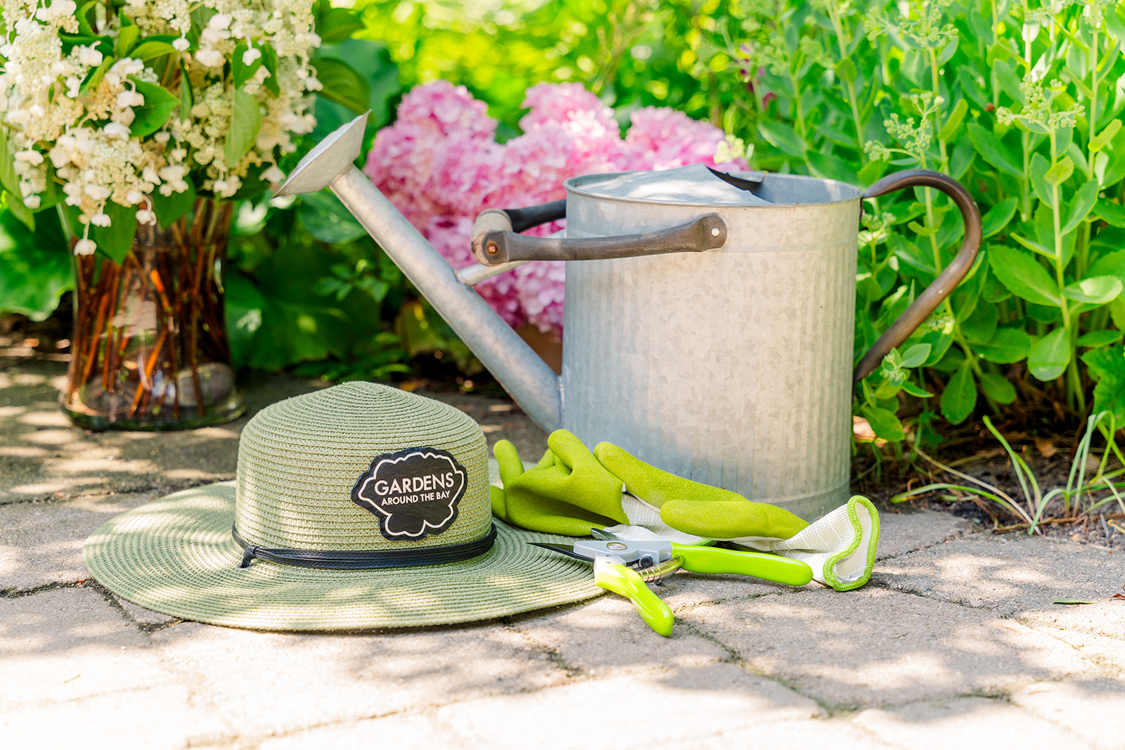 Garden's by the bay hat, watering can, garden gloves on the pavement.