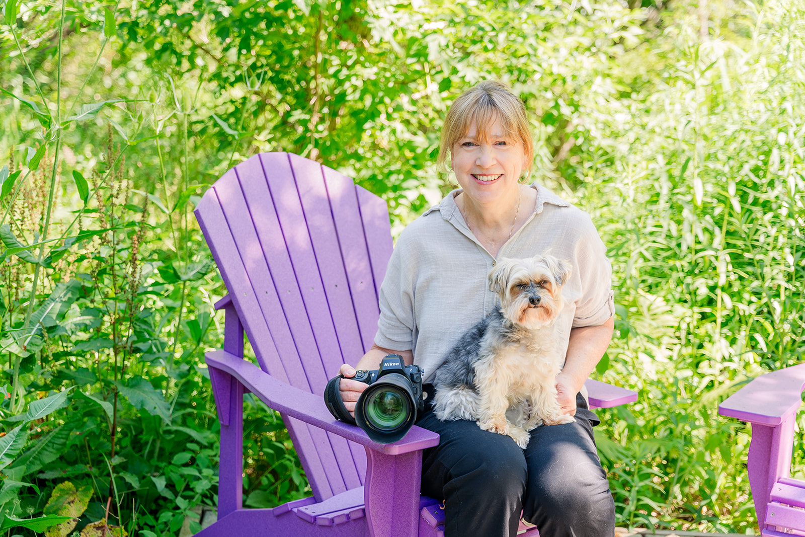 Kelly Borgers posing on a purple chair with a dog and her camera in hand.